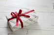 A gift box with a red ribbon wrapped in musical note wrapping paper placed on a white wooden table
