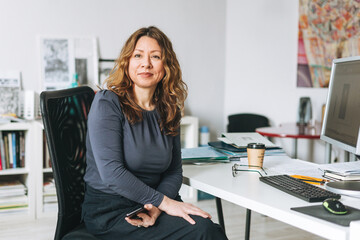 Charming smiling adult woman middle aged with curly hair architect designer manager working in bright modern office