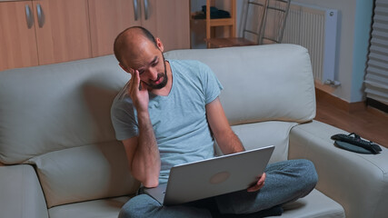 Poster - Tired man sitting on sofa while talking with collegue during business videocall conference using laptop computer, Caucasian male working from home because of coronavirus quarantine late at night