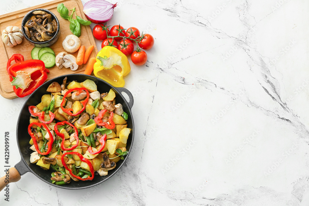 Frying pan with tasty vegetables, chicken and ingredients on light background