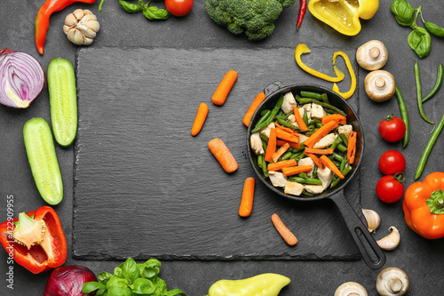 Obraz Dibond Composition with frying pan, tasty vegetables, chicken and ingredients on dark background