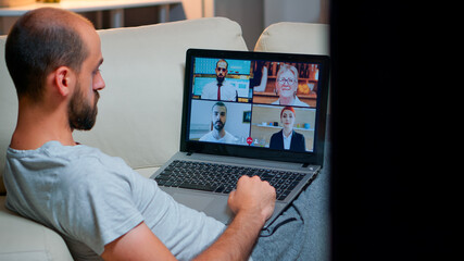 Poster - Over shoulder view of man in pajamas having online conversation with teammates working at online technology project using laptop computer, videoconference web internet communication