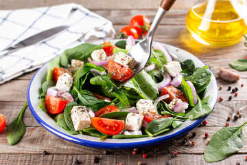 Wall Mural - Spring vegan salad with spinach, cherry tomatoes, baby spinach, feta cheese and red onion on a rustic wooden table. Healthy food concept.