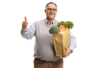 Canvas Print - Cheerful mature man holding a grocery bag with healthy food and showing thumbs up