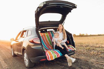 Wall Mural - Happy family, a young mother with a child sitting in the trunk of a car, traveling