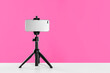 Smartphone fixed to tripod on white table against pink background. Space for text