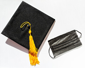 Canvas Print - Black graduate cap with yellow tassel and protective face mask on white background, protection from virus while studying, getting diploma in new reality, new normal, Flat lay, top view, mortarboard