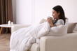 © New Africa - Woman covered in blanket holding cup of drink on sofa, space for text