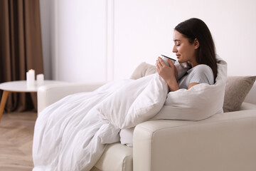 Wall Mural - Woman covered in blanket holding cup of drink on sofa, space for text