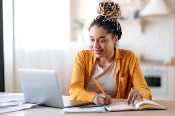 focused cute stylish african american female student with afro dreadlocks, studying remotely from ho