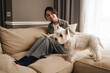 © Drobot Dean - Happy white woman reading book while resting with her dog on sofa