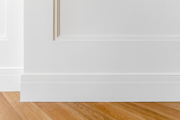 Fragment of classic white interior with wooden french herringbone parquet floor and installed wall panels, decorated with moldings and skirting boards. Final stage of finishing works in the apartment