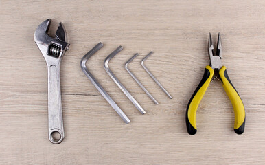 Adjustable wrench, different sized hex wrenches and wire cutters on a wooden background. Various tools on a wooden table