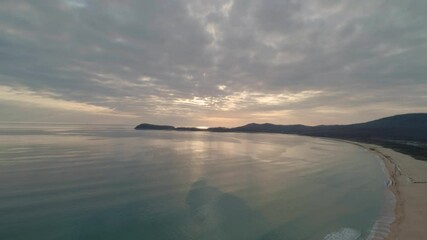 Wall Mural - Aerial view of beach with calm transparent sea water and sky reflection at sunset. Camera moves backwards