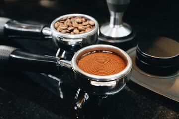 Close-up of portafilter with coffee beans, roasted, ground, and hot coffee and tamper, equipment for making freshly brewed coffee