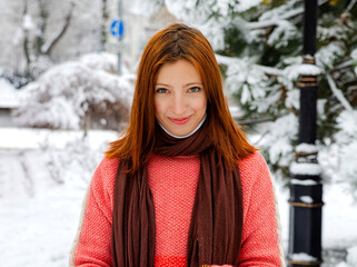 A red-haired girl in a red sweater against the snow. A walk in winter. Playing with snow