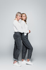 full length view of middle aged woman hugging young, trendy daughter on grey