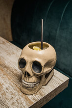 Ceramic Polynesian Tiki Cup Skull Shaped With Straw Placed On Wooden Table On Blurred Background