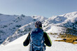 © Sergio Victor Vega/ADDICTIVE STOCK - Back view of unrecognizable male mountaineer in warm activewear with backpack standing on slope of snowy rocky mountain and enjoying spectacular landscape in sunny winter day