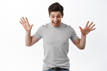 Portrait of excited man raise hands and look amazed down, found something on floor, standing happy against white background