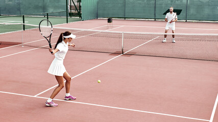 Sticker - Pretty girl plays tennis on the court outdoors. She prepares to beat on a ball. Woman wears a light blue sportswear with white sneakers