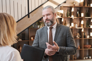 Wall Mural - Mature bearded businessman talking to employee while they standing at office