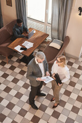 Wall Mural - High angle view of business couple discussing financial report and preparing for a meeting with African businessman working on laptop in the background