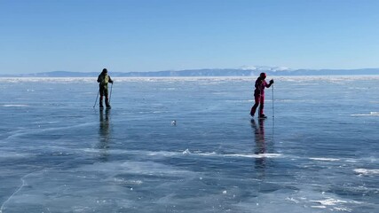 Wall Mural - Ice skating across Lake Baikal. A guy and a girl are skating and with ski poles on the ice of the frozen Lake Baikal. A beautiful winter landscape with clear, smooth blue transparent ice and deep crac