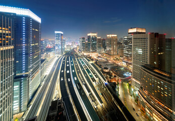 Wall Mural - Beautiful nightscape of Tokyo Train Station with a high angle view of railway platforms stretching between modern office towers & city lights glistening under blue evening sky in Chiyoda, Tokyo, Japan