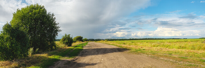 Sunny summer landscape with dirt rural road passing through the fields and meadows.