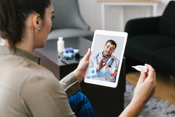 Latin woman talking with a doctor online using digital tablet and computer, feeling bad at home. Concept of telemedicine and patient in Mexico city