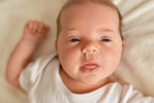 Newborn Boy Or Girl Having Runny Nose And Snot, Infant Wearing White Bodysuit Or T Shirt Looking Away, Lying On White Blanket, Child's Healthy Problem.