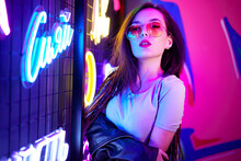 Fashion Portrait Of A Young Woman In Sunglasses Posing Near Neon Signs In Night Club