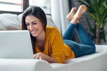 Pretty Young Woman Working With Her Laptop While Lying On Couch At Home.
