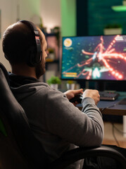 Wall Mural - Cyber man with headset playing game in competition holding wireless controller in professional equiped studio. Excited player sitting on gaming chair looking at monitor for winning online championship