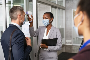 Businesswoman using infrared thermometer before letting people into the office