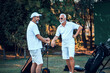 Two older men stand on a golf course and talking.