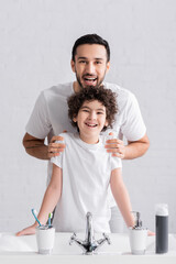 Wall Mural - Happy father hugging arabian son near toiletries in bathroom