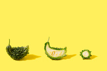Three PieThree Pieces Of Unique Bitter Gourd Veggie, Whole, Half Of It And Small Slice On Yellow Background.se Of Unique Bitter Melon Veggie, Half Of It And Small Slice On Yellow Background.