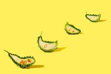 Four Slices Of Bitter Gourd On Vibrant Yellow Background.