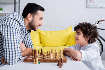 Wall Mural - Side view of muslim man smiling at son near chess on board