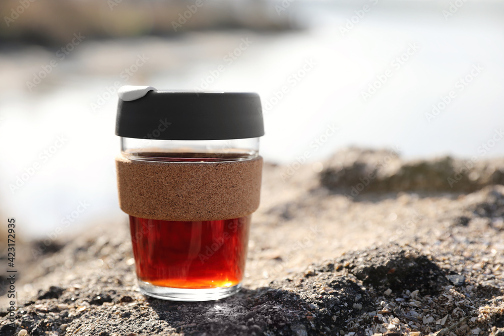 Reusable glass cup with hot drink on rock stone outdoors. Space for text - obrazy, fototapety, plakaty 