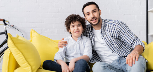 Wall Mural - young muslim man embracing happy son while looking at camera, banner