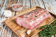 Raw Whole boneless pork loin meat with thyme and salt on rustic board. White wooden background. Top view
