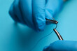 © New Africa - Professional surgeon holding forceps with suture thread on light blue background, closeup. Medical equipment