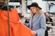 © antgor - Woman chooses an orange dress in the store before buying