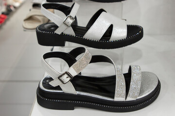 Fashionable comfortable silver leather women's sandals with rhinestones, with a small heel on the counter of a boutique store.