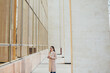 © eduard - Young pretty woman with eyeglasses near office with panoramic windows drink the coffee at break.