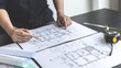 © Puwasit Inyavileart - Architectural building design and construction plans with blueprints, Young man was designing a building or architecture with a ruler, pen, pencil, tape measure, architect hat.