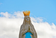 Detail Of The Statue Of The Virgin Mary In Lourdes In Front Of A Cloudy And Blue Sky: "our Lady Of Lourdes"